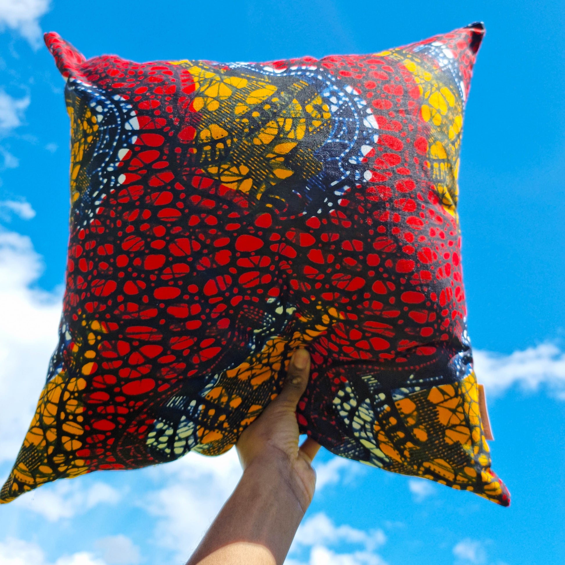 Large Osime Home Eno Cushion held up in the bright blue sky with clouds in the background.