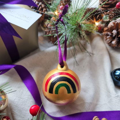 Osime Home Pan African Bauble hand painted design surrounded by pine cones and purple ribbon.